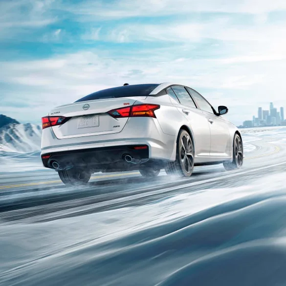 2027 Nissan Altima in white seen from behind driving in snowy landscape illustrating all-wheel drive at Rob Green Nissan in Twin Falls ID